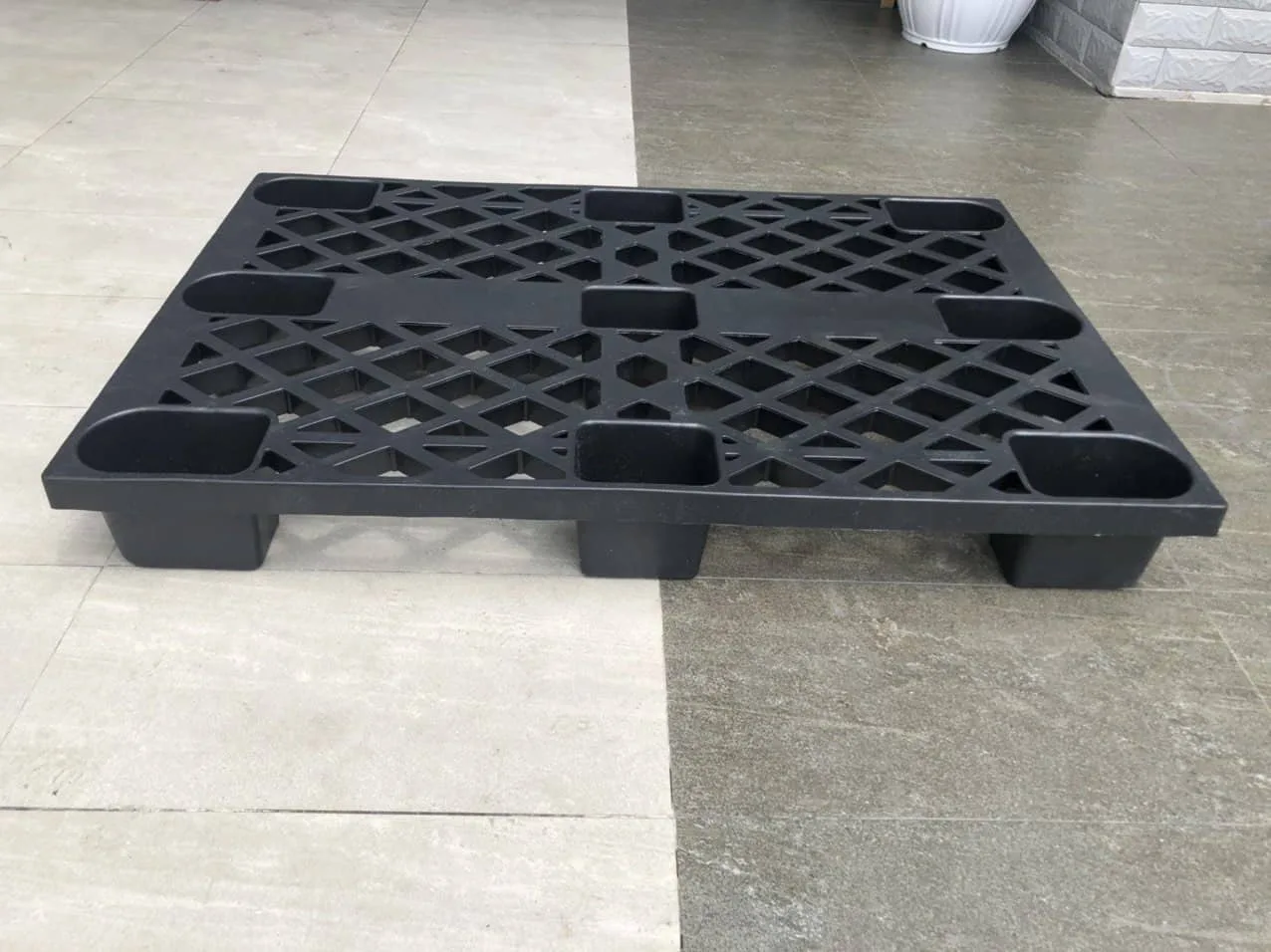 Black cup-foot plastic pallet, 1200 x 800 x 140 mm, on a tiled floor