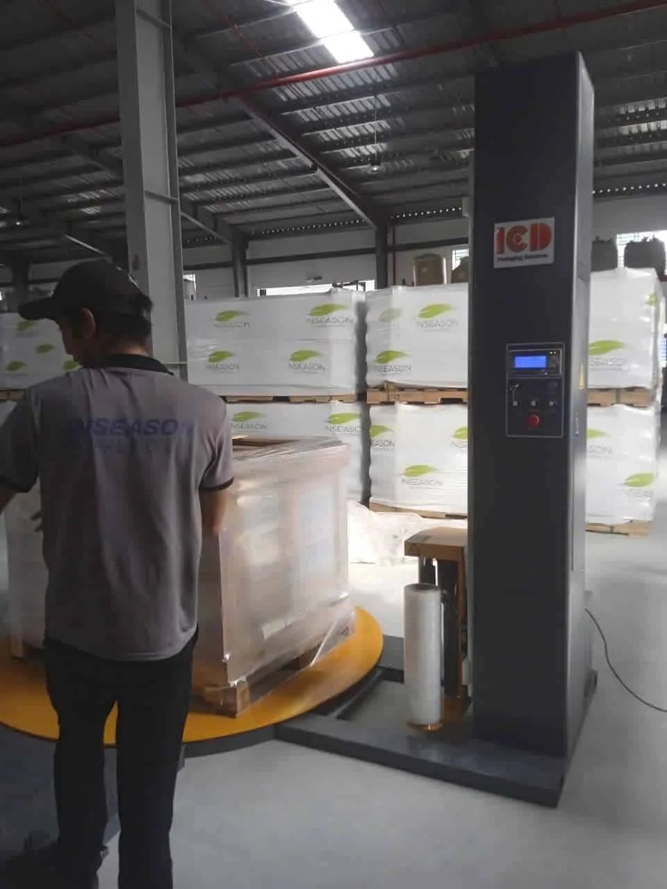 Nhân viên đứng cạnh máy quấn màng mâm xoay ICD và pallet hàng đang được quấn màng tại kho khách hàng