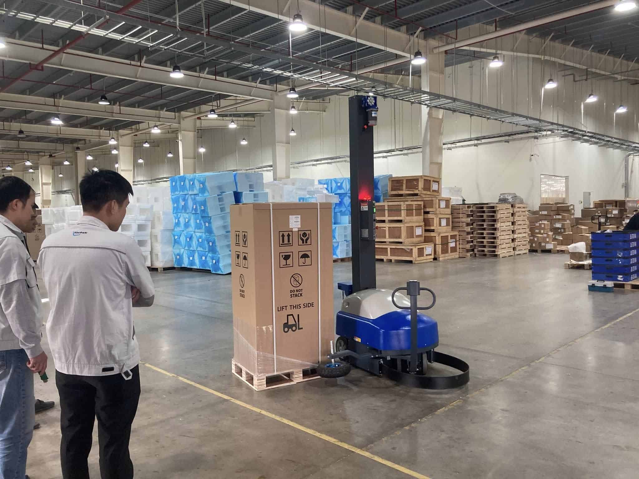Robot quấn màng tự động quấn pallet hàng trong kho, nhân viên khách hàng đứng xem