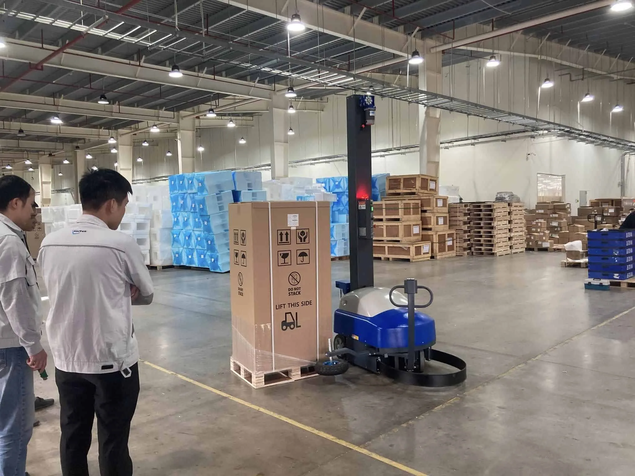 Battery-powered mobile wrapping robot beside a pallet of cartons in a customer's warehouse