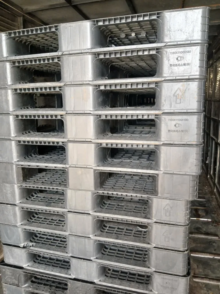 Pallet nhựa màu xám xếp chồng, cận cảnh ký hiệu kích thước đúc trên thân pallet