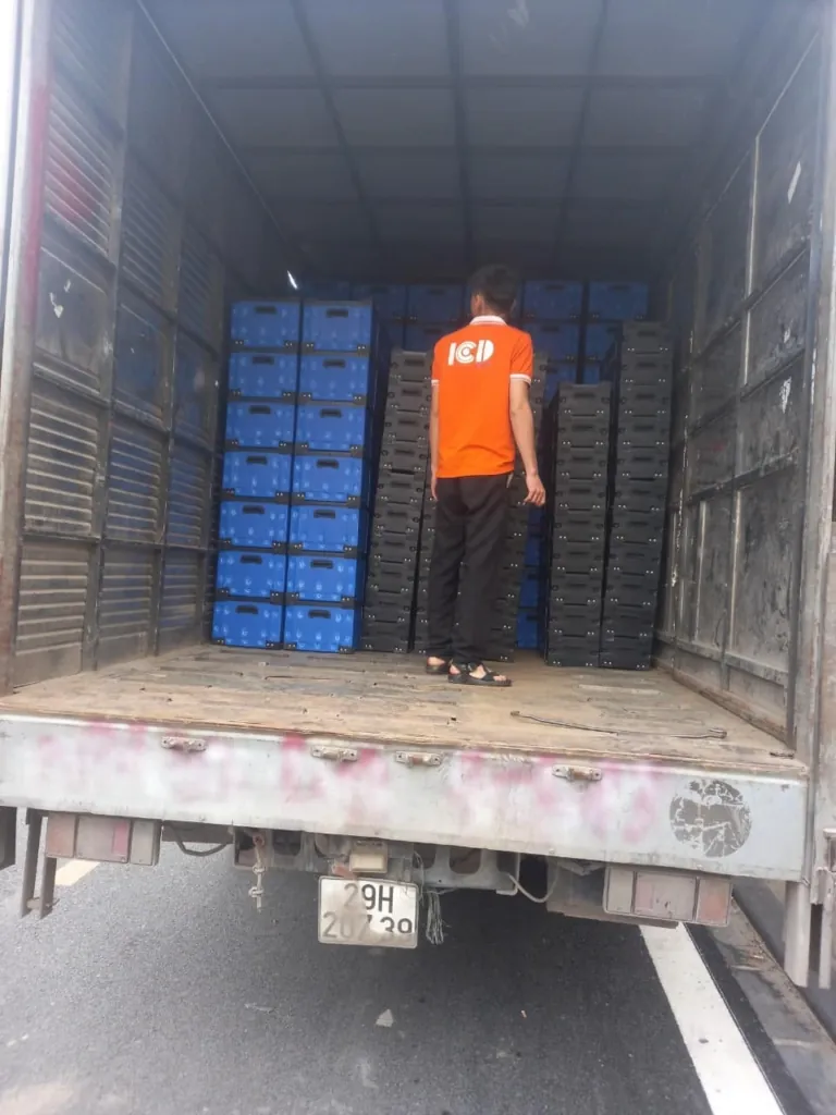 Thùng nhựa xanh dương và pallet nhựa đen xếp trong thùng xe tải giao hàng