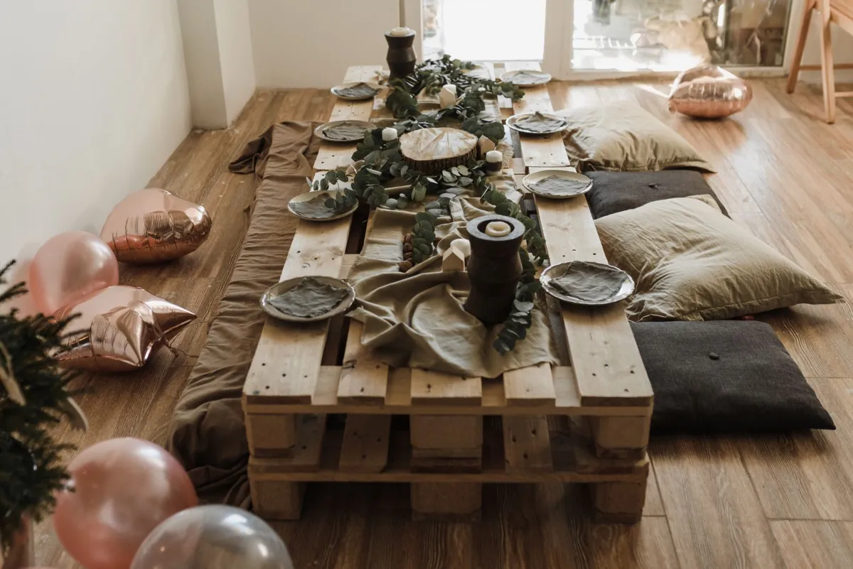 A low table made from two stacked wooden pallets, set with dishes and candles among floor cushions