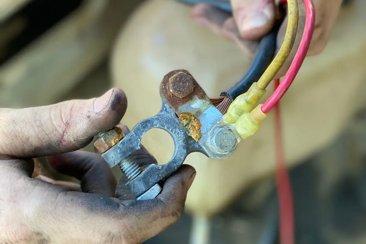 Oxidised battery terminals connected to yellow and red cables in a technician's hand