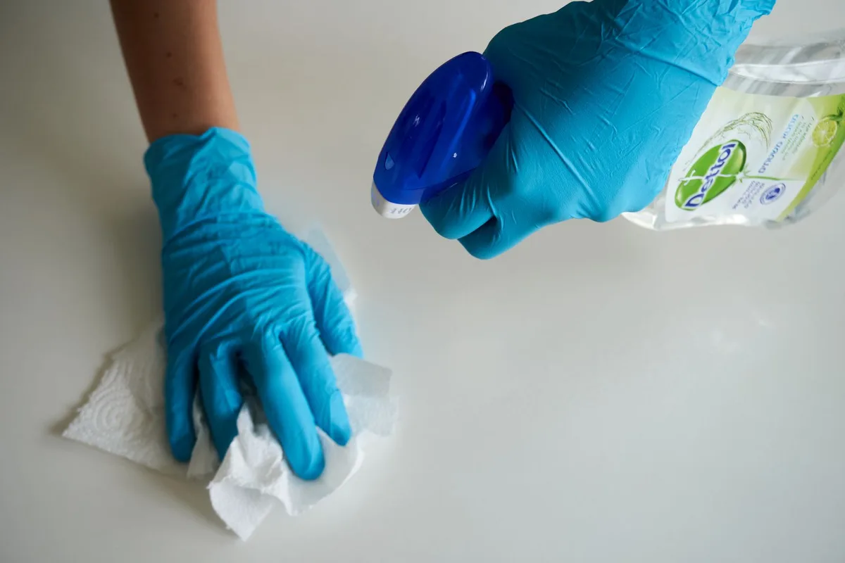 Two gloved hands spraying disinfectant solution and wiping with a paper towel