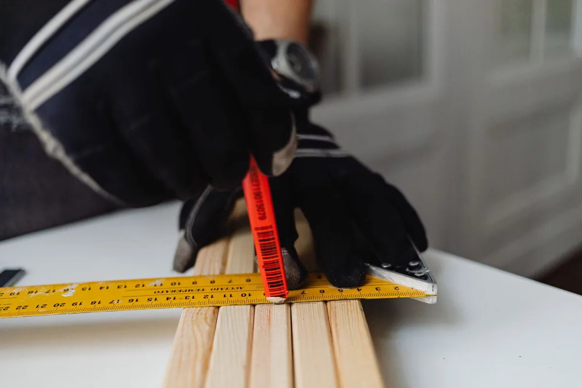 A worker using a tape measure and pencil to mark a timber strip before cutting