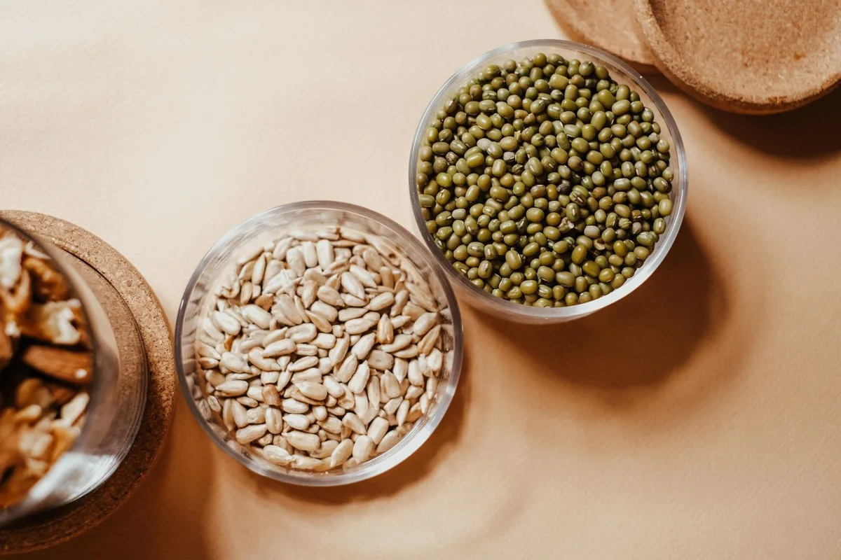 A glass bowl of whole mung beans next to other kinds of beans