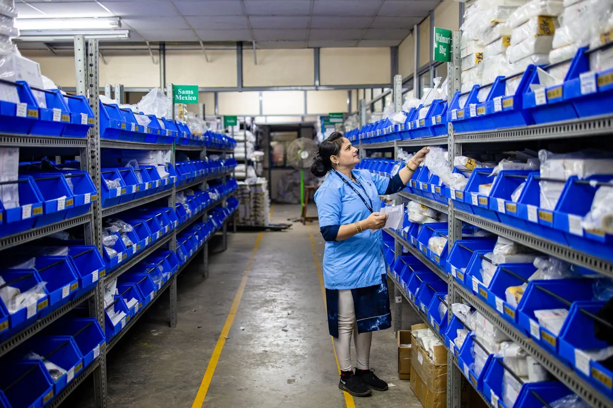 A worker picking goods from blue plastic bins stacked on warehouse shelves