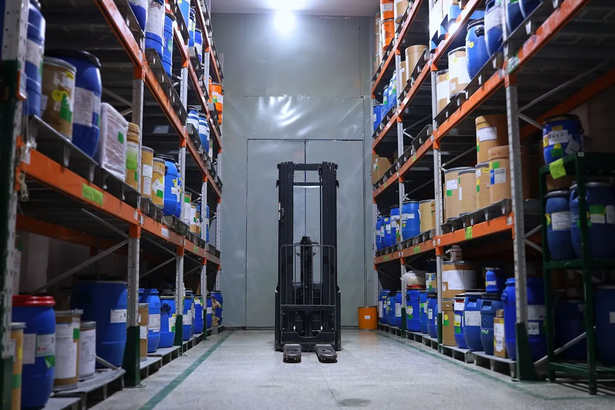 Pharmaceutical raw material store with drums and packaging on racks and a forklift in the aisle