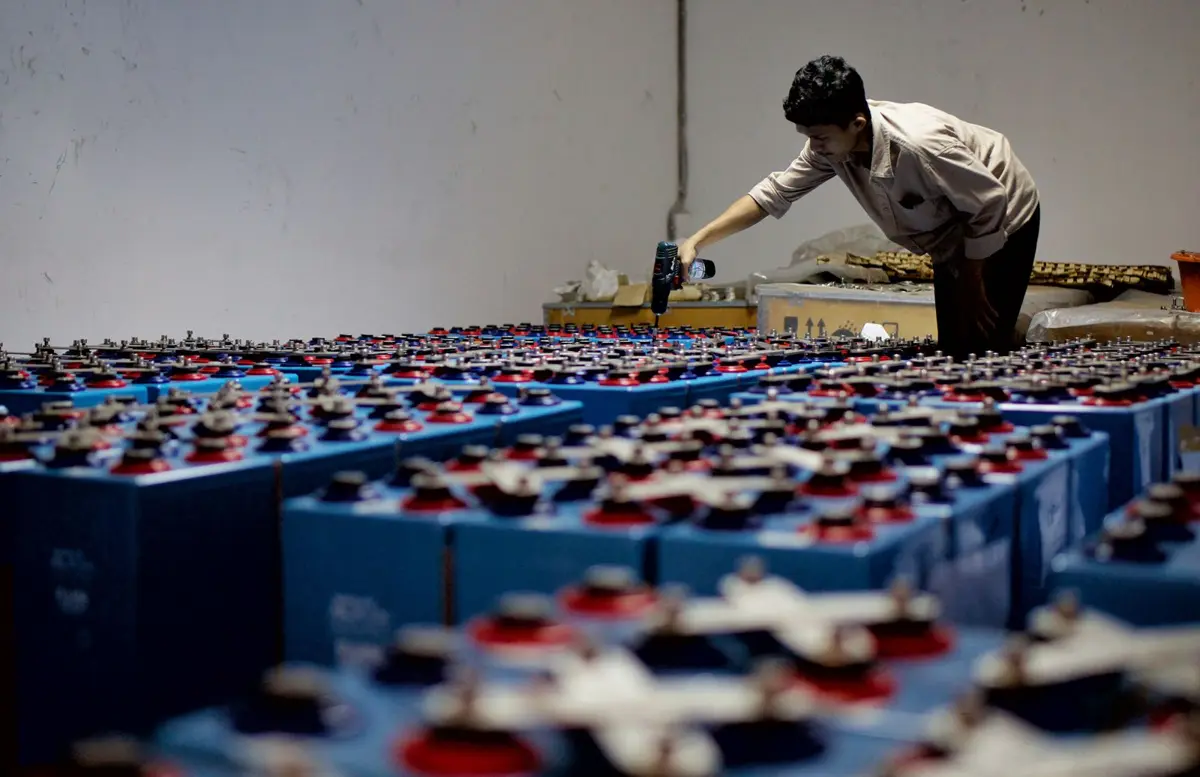 Workers using handheld equipment to inspect a row of batteries lined up in a warehouse