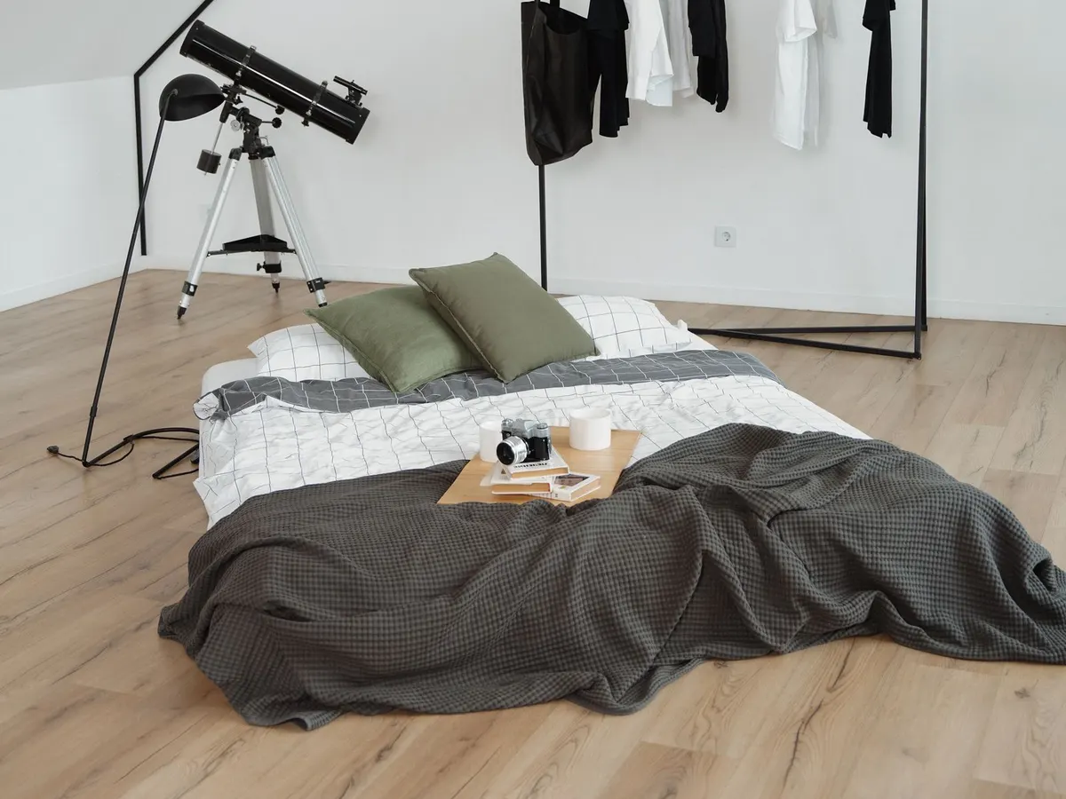 A mattress with grey sheets laid directly on a wooden floor in a minimalist bedroom