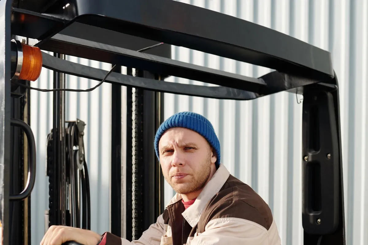 Forklift operator seated under the overhead guard, with the mast behind
