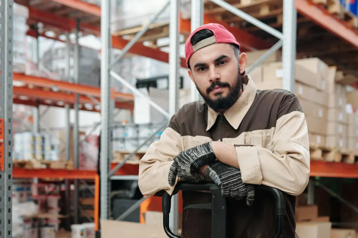 Warehouse worker in gloves standing beside the handle of a hand pallet truck between rows of racking