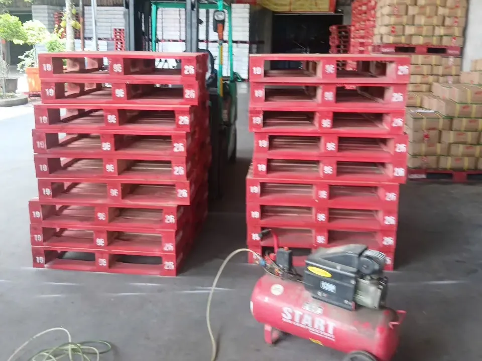 Red painted wooden pallets with numbered stringer boards stacked in two piles in a warehouse