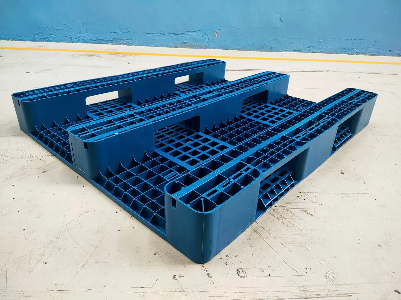 Underside of a blue three-runner plastic pallet, with fork openings cut through each of the three runners