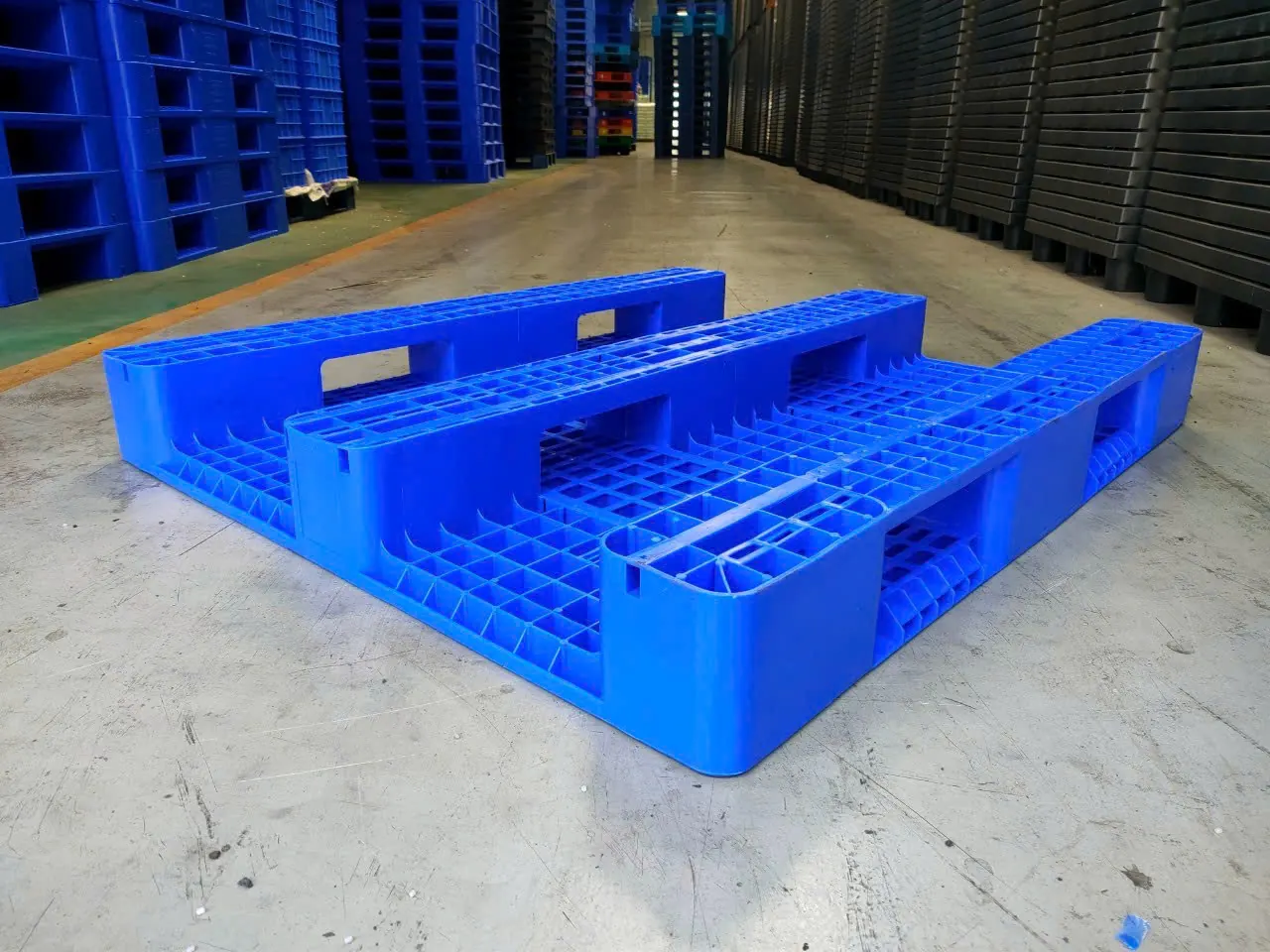 Mặt dưới pallet nhựa 3 chân màu xanh dương, ba thanh đáy chạy suốt chiều dài là vị trí bắt bánh xe