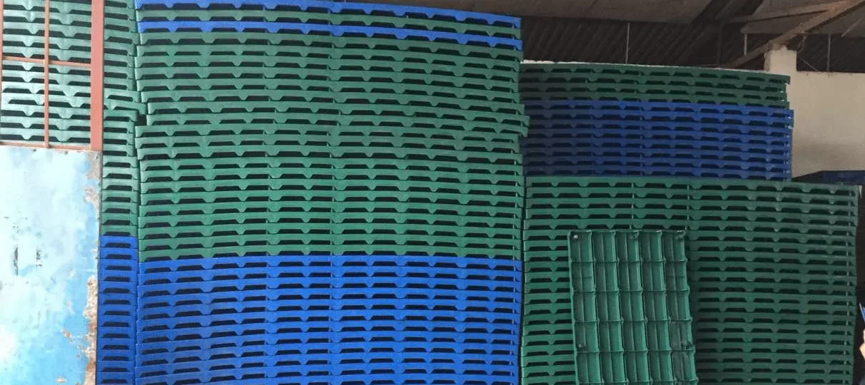 Hàng trăm tấm pallet nhựa lót sàn mặt nan màu xanh dương và xanh lá xếp chồng cao trong xưởng