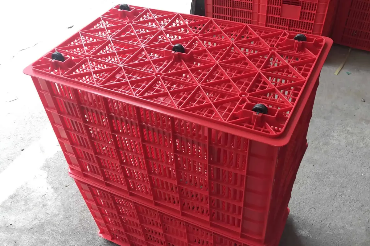 Two red plastic crates with wheels stacked, the upper crate upside down showing the wheels under the base