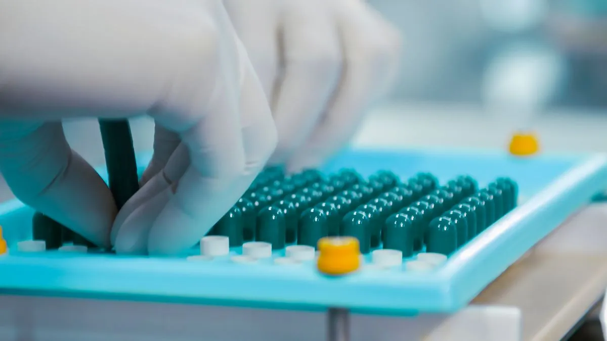 A gloved hand placing capsules on a tray in a pharmaceutical laboratory