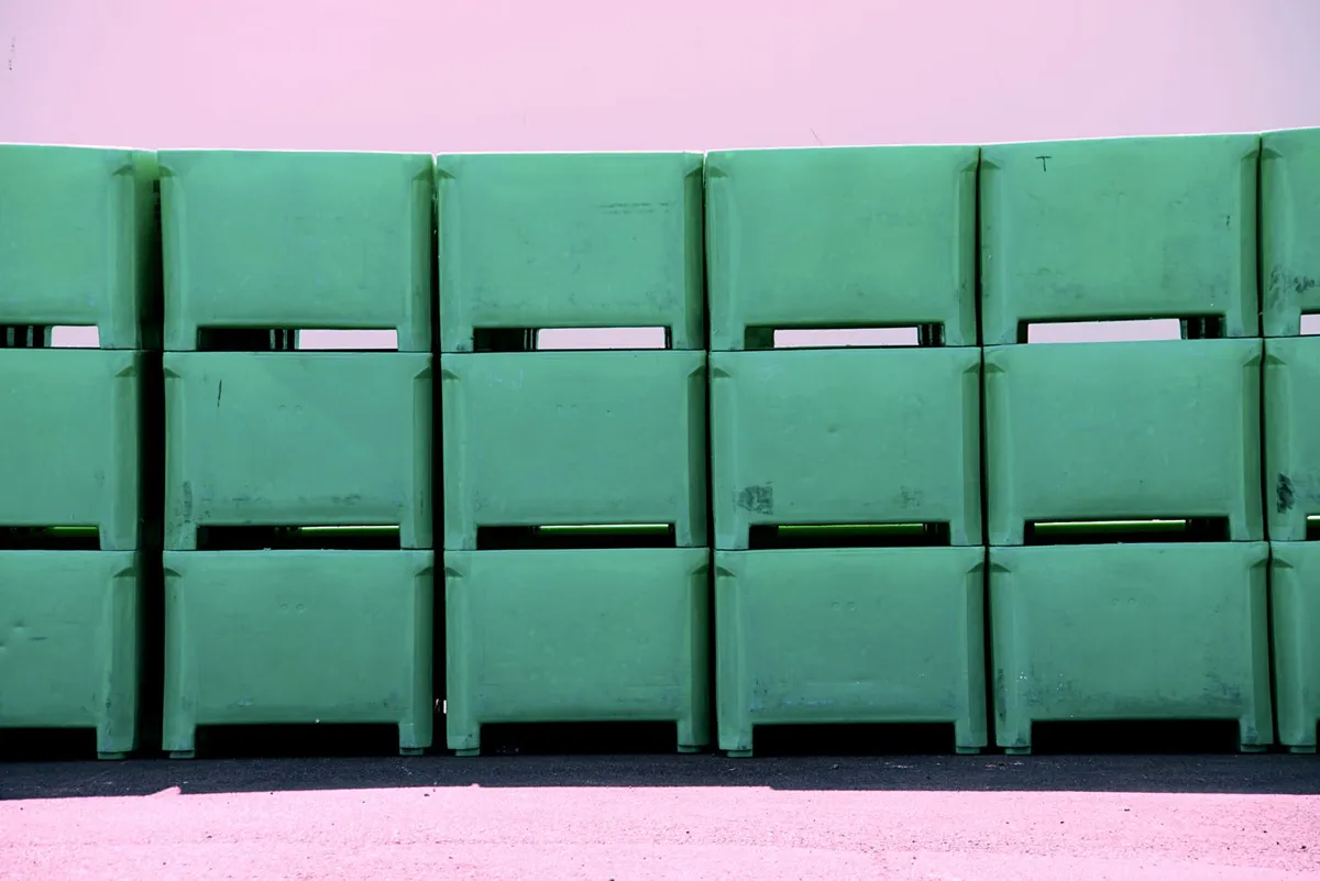 Several large green plastic bins stacked three high on their feet, with gaps between the tiers