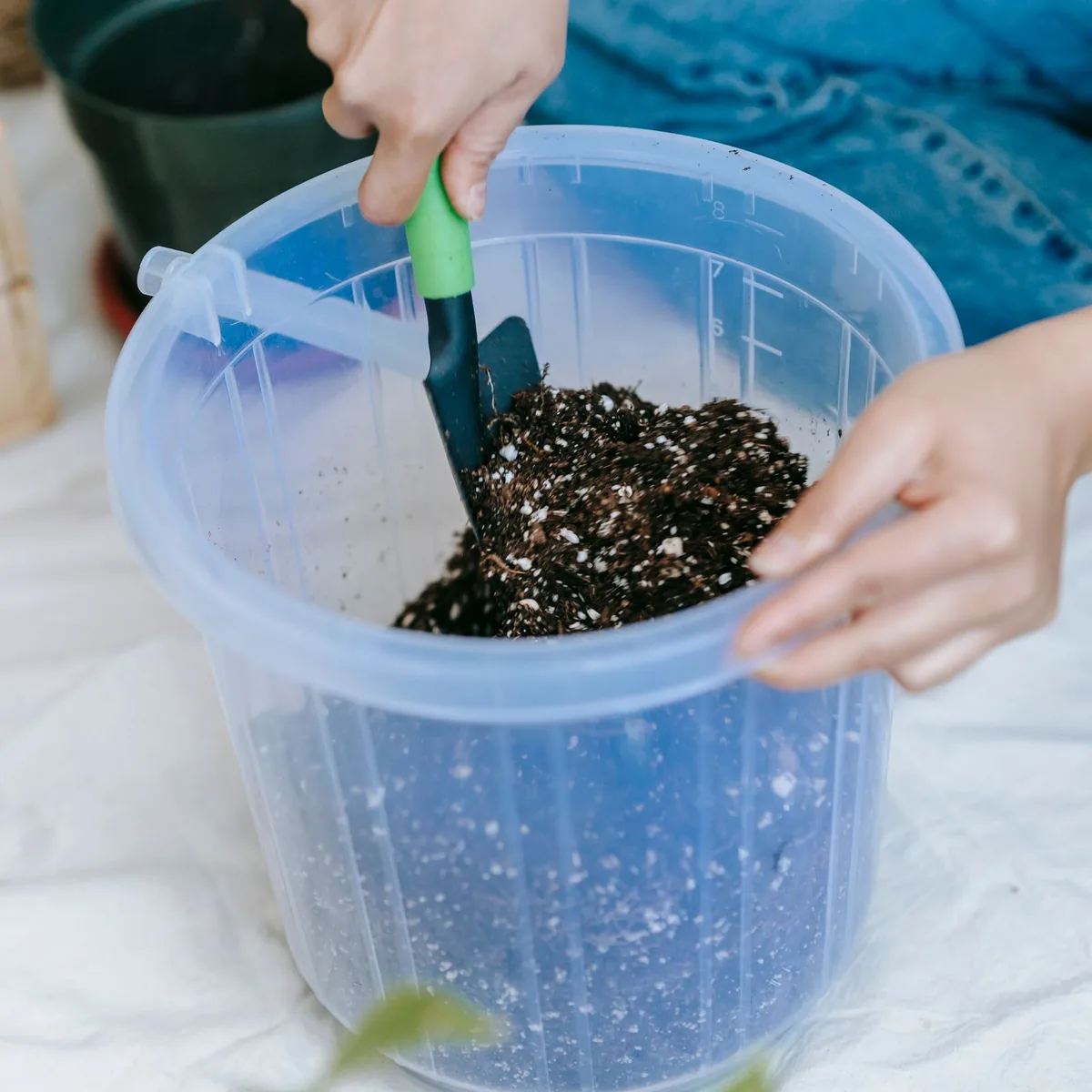 Gloved hand mixing soil with perlite in a clear plastic bucket