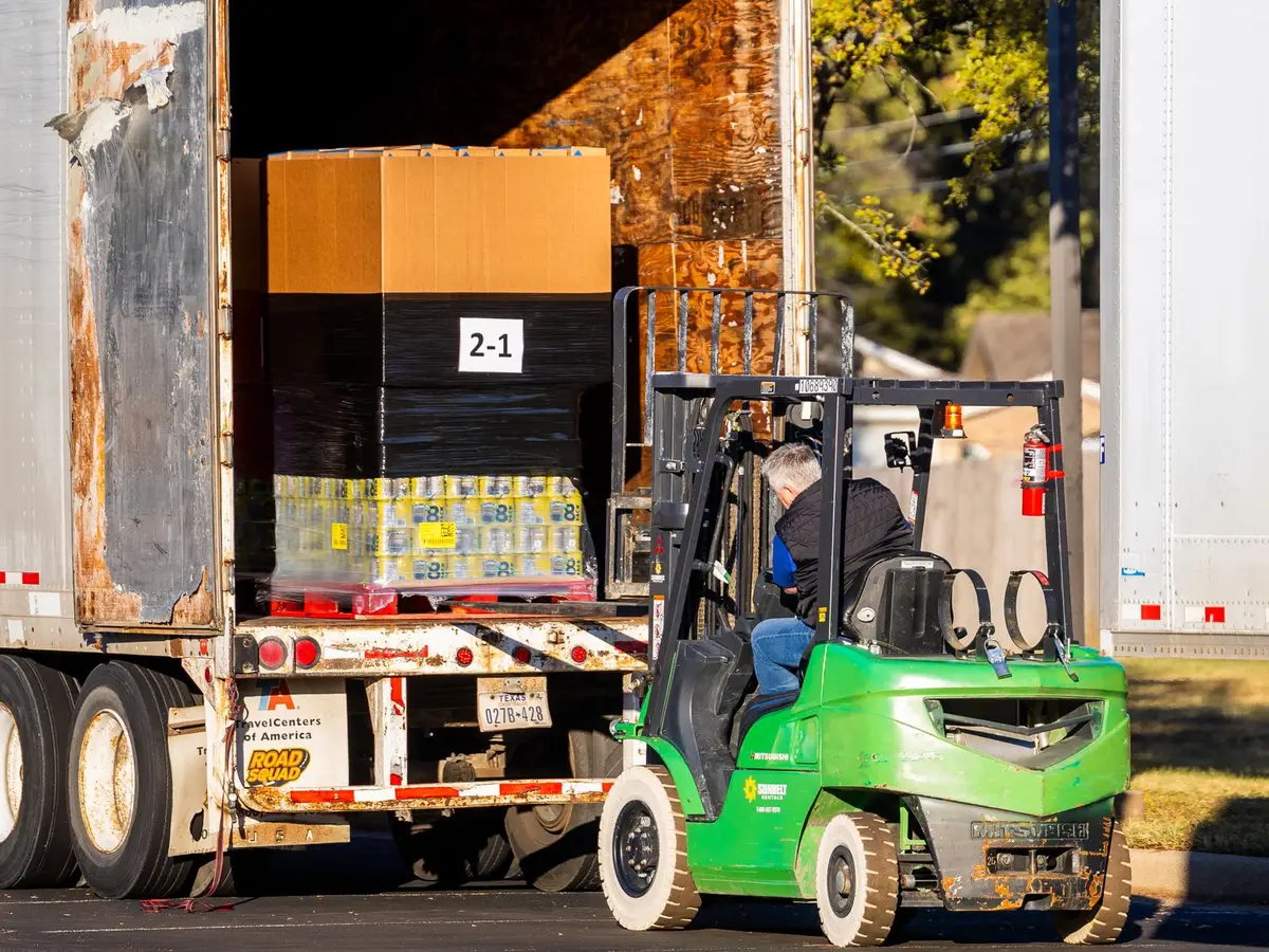 Xe nâng màu xanh lá đưa pallet hàng vào thùng xe tải
