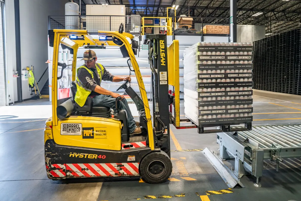 Forklift placing a package on a pallet onto a roller conveyor in a warehouse