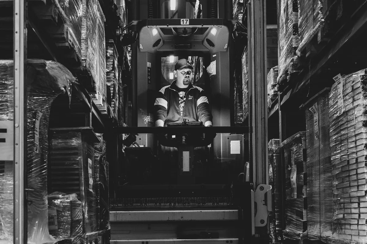Ride-on forklift working in a narrow aisle between two rows of racking full of stretch-wrapped pallets
